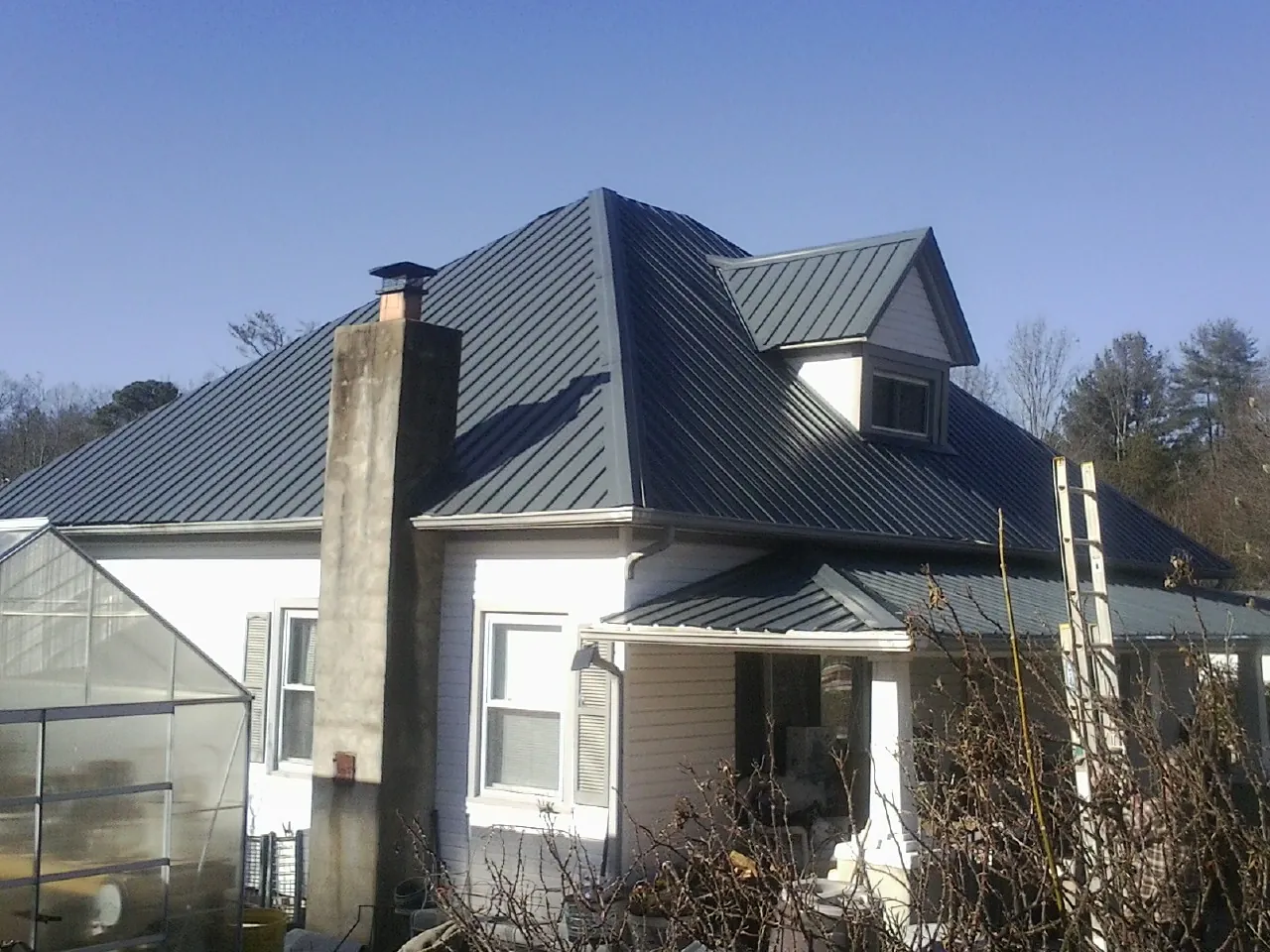 Dark blue standing seam metal roof on a white farmhouse with dormer — Slate & Tile Roof Repair by Roofing Brothers in Irvona