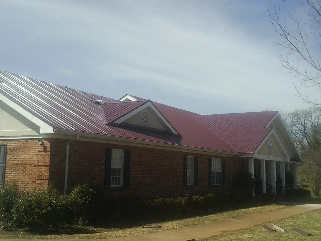 Red metal roof with gabled entries on a long brick building, from a Hail Damage Roof Repair job in Irvona