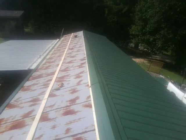 Old rusted panels beside newly installed green metal roofing — Wind Damage Roof Repair by Roofing Brothers in Irvona