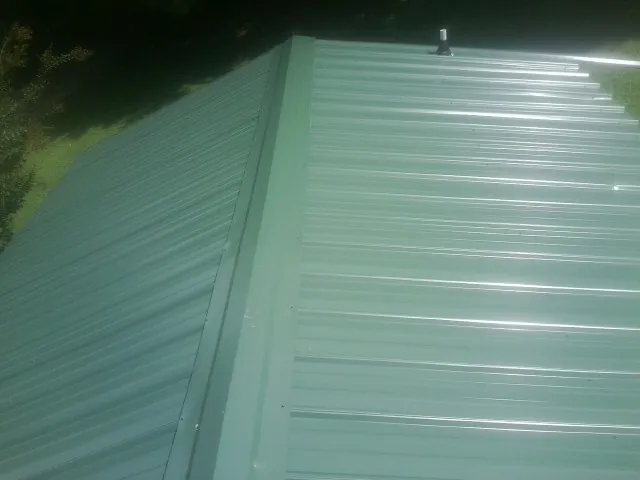 New green metal panels meeting at the ridge of a roof — Flat Roof Repair work by our crew in Irvona