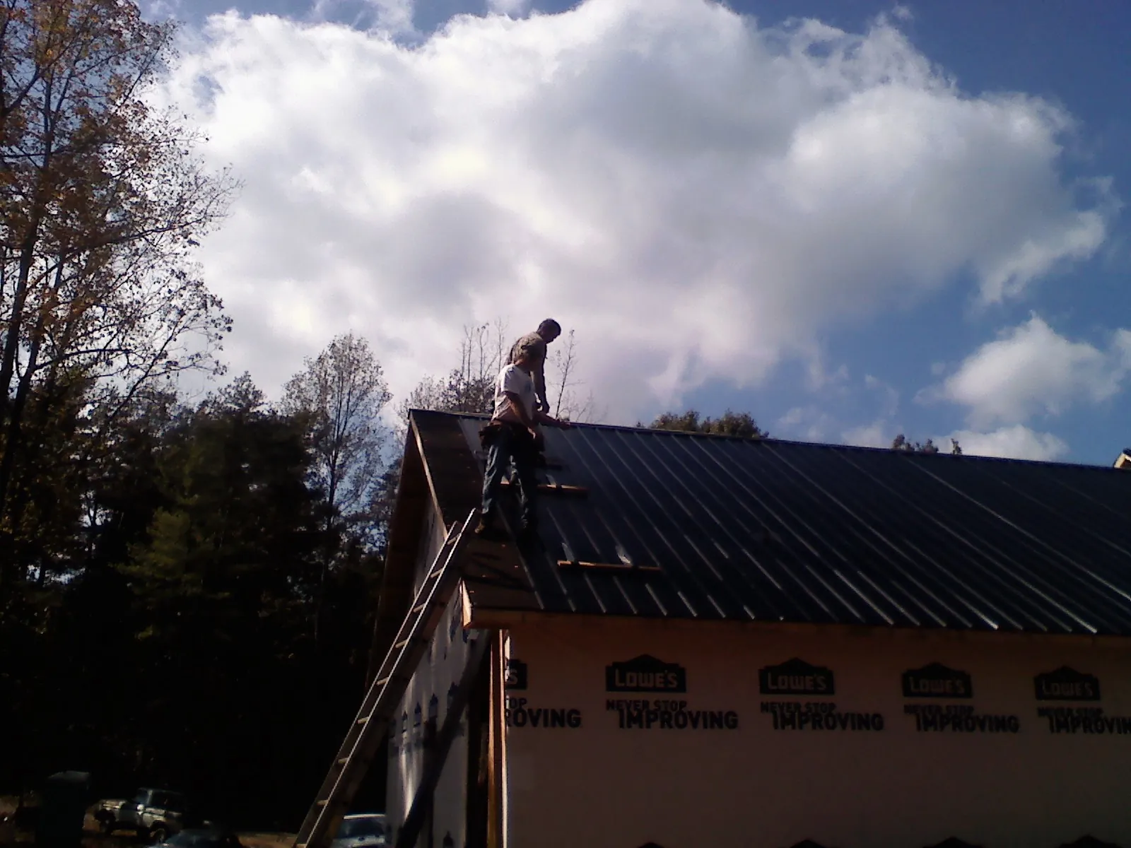Roofer fastening dark metal panels high against a cloudy sky, from a Roof Inspection job in Irvona