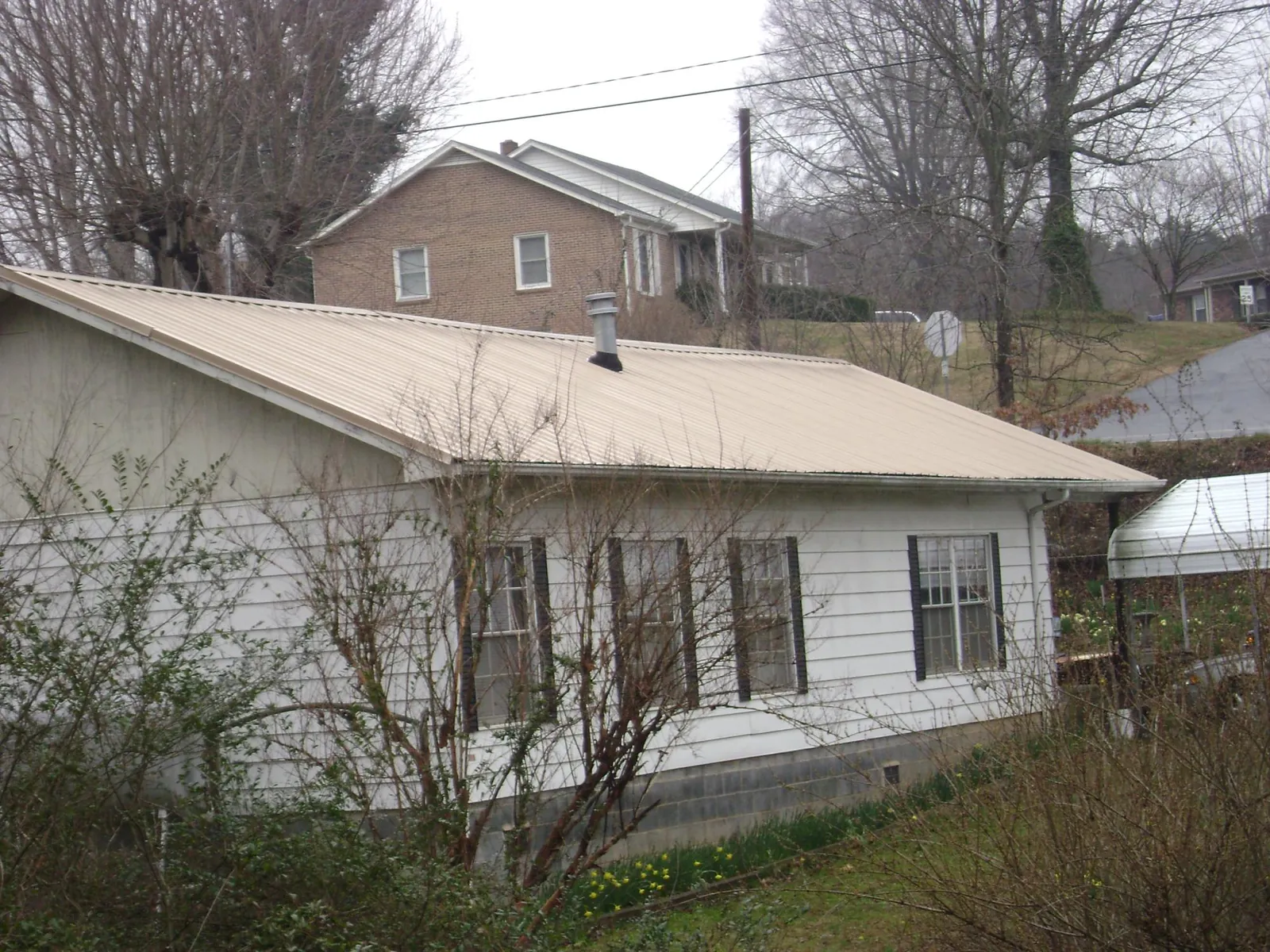 Tan metal roof on a white sided house set into a hillside — Commercial Roofing by Roofing Brothers in Irvona