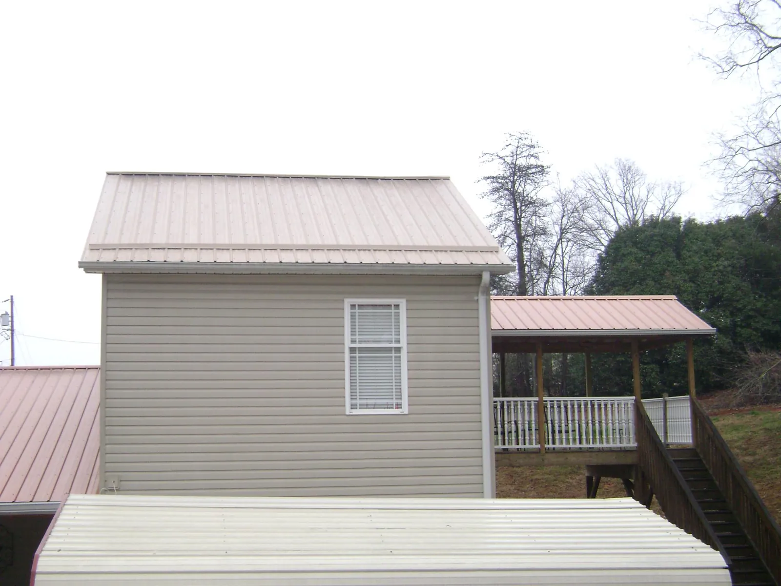 Tan metal roofs on a two story addition and attached porch, from a Roof Replacement job in Irvona
